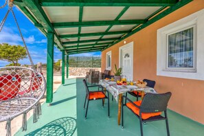 A covered outdoor dining area with a table set for two, chairs, and a hanging chair.