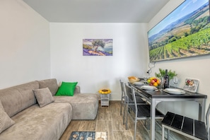 A living room with a sofa, a dining table set for two, a small side table, and a painting on the wall.