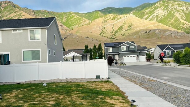 A residential street with houses, a white fence, and a grassy area. - Cozy Hideaway Parks + Trails Near SLC Airport (Lake Point)