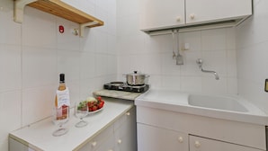 Cuina amb armaris blancs, una prateleira de fusta, fogó, vàter i ampolla de vi.