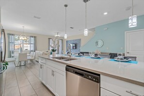 Une cuisine moderne avec des meubles blancs, un lave-vaisselle en acier inoxydable et des luminaires suspendus.