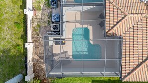 Vue aérienne d’un espace piscine sur le toit, doté d’une structure en verre, de deux unités de climatisation et d’un toit recouvert de tuiles.