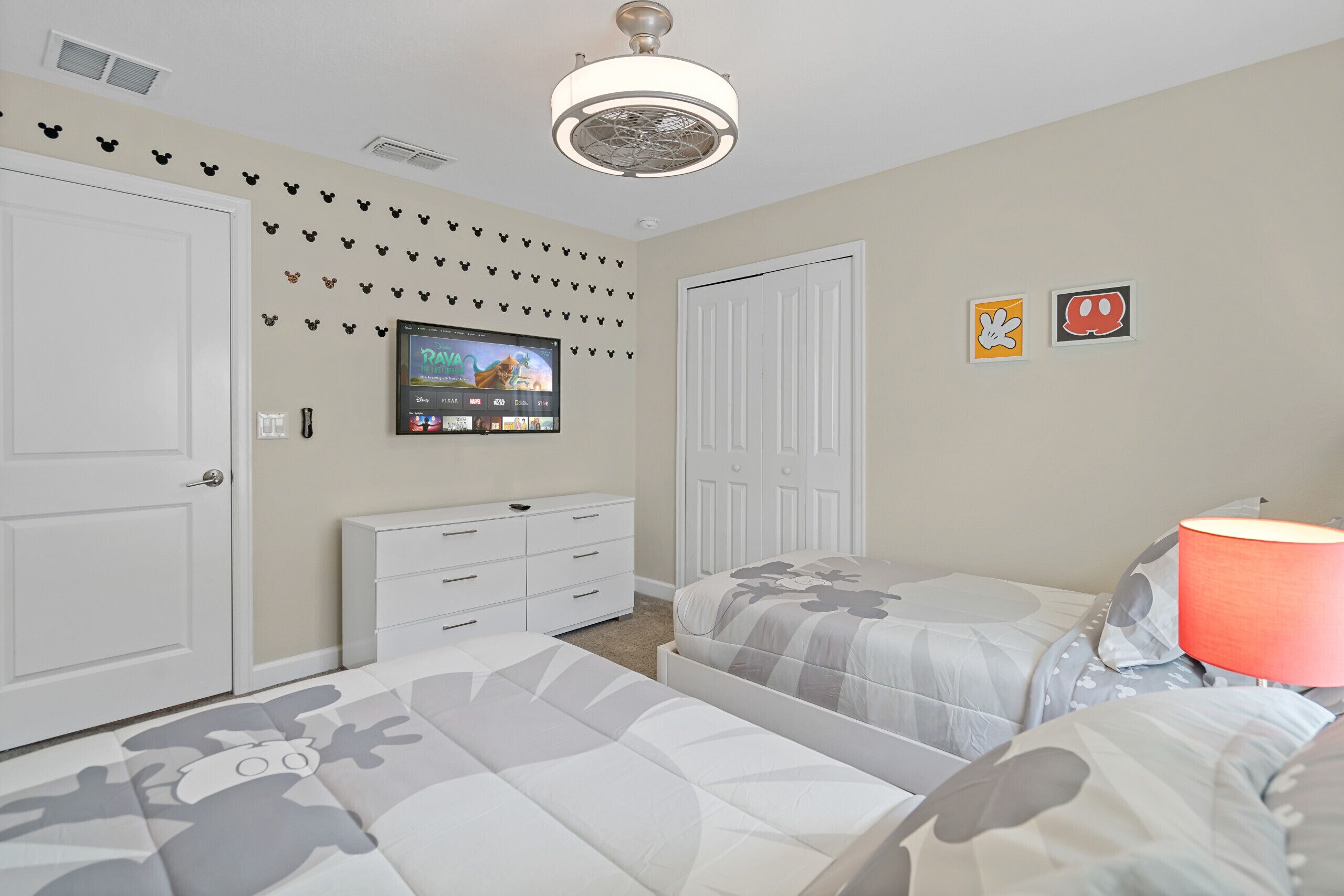 A bedroom with two beds, a TV mounted on the wall, and a dresser.