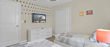 Un dormitorio con dos camas, un televisor montado en la pared y un aparador.