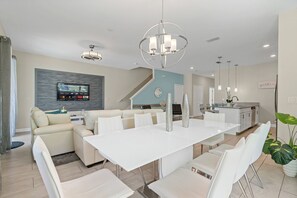Uma sala de estar moderna com área de jantar, televisão na parede e cozinha ao fundo.