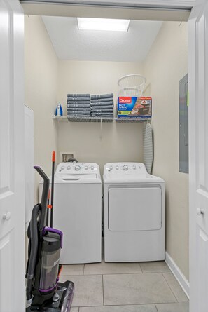 A laundry room with two front-loading washing machines, a stacked drying rack, and a vacuum cleaner.
