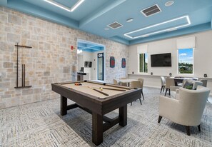 A pool table in a room with stone walls, a billiards rack, and a seating area with chairs and a table.