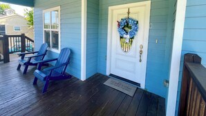 A porch with two blue Adirondack chairs, a white door with a blue wreath, and a welcome mat.