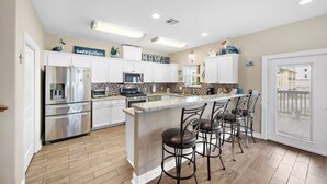 A spacious kitchen with white cabinets, stainless steel appliances, and a central island with bar stools.