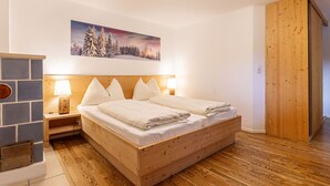 Un dormitorio con una cama de madera, ropa de cama blanca, una mesita de noche con una lámpara, un cuadro de un paisaje nevado y un armario de madera.
