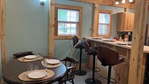A dining area with a wooden table set for four, surrounded by bar stools, and a kitchen area with wooden cabinets and a countertop.