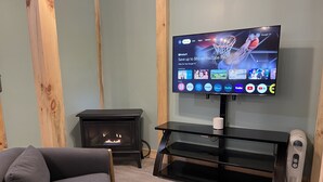 A living room with a TV mounted on the wall displaying various streaming services, a black entertainment unit, a fireplace, and a gray sofa.