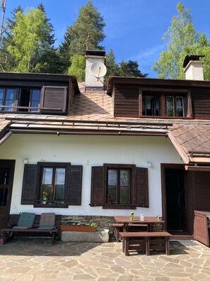 A rustic building with a stone patio, wooden furniture, and a satellite dish. - Gallys Mounting Cottage Pod Boubinem with WiFi (Lenora)