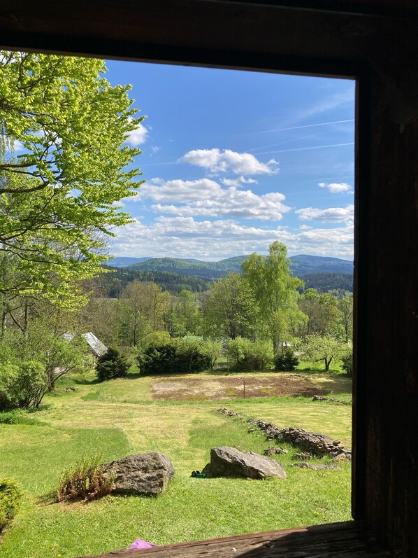 A view through a window of a grassy field with scattered rocks, trees, and distant mountains.