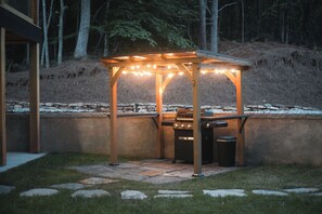 Un espace extérieur aménagé en terrasse, avec une pergola, un barbecue et une poubelle.