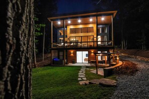 Une maison moderne à deux étages, dotée d’un balcon, d’un chemin en pierre et d’un espace extérieur aménagé pour se détendre.