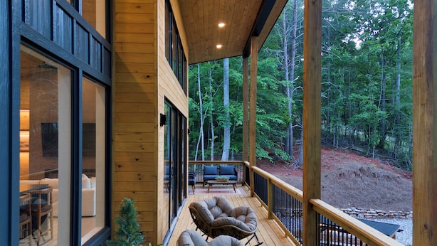 Une terrasse en bois avec deux fauteuils rembourrés et un canapé, donnant sur une zone boisée.