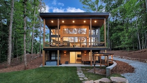 Une maison moderne à deux étages, avec une façade en bois, de grandes fenêtres et un espace extérieur aménagé avec des sièges.