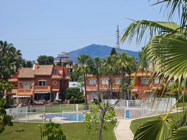 A hotel with a swimming pool, palm trees, and a mountain in the background.