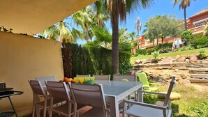 An outdoor patio with a table and chairs, surrounded by palm trees and a stone wall.