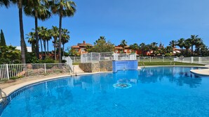 A swimming pool with a stone wall and a sign, surrounded by palm trees and a fence.