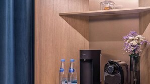 A hotel room with a wooden shelf containing a water dispenser, a coffee machine, and a vase with flowers.