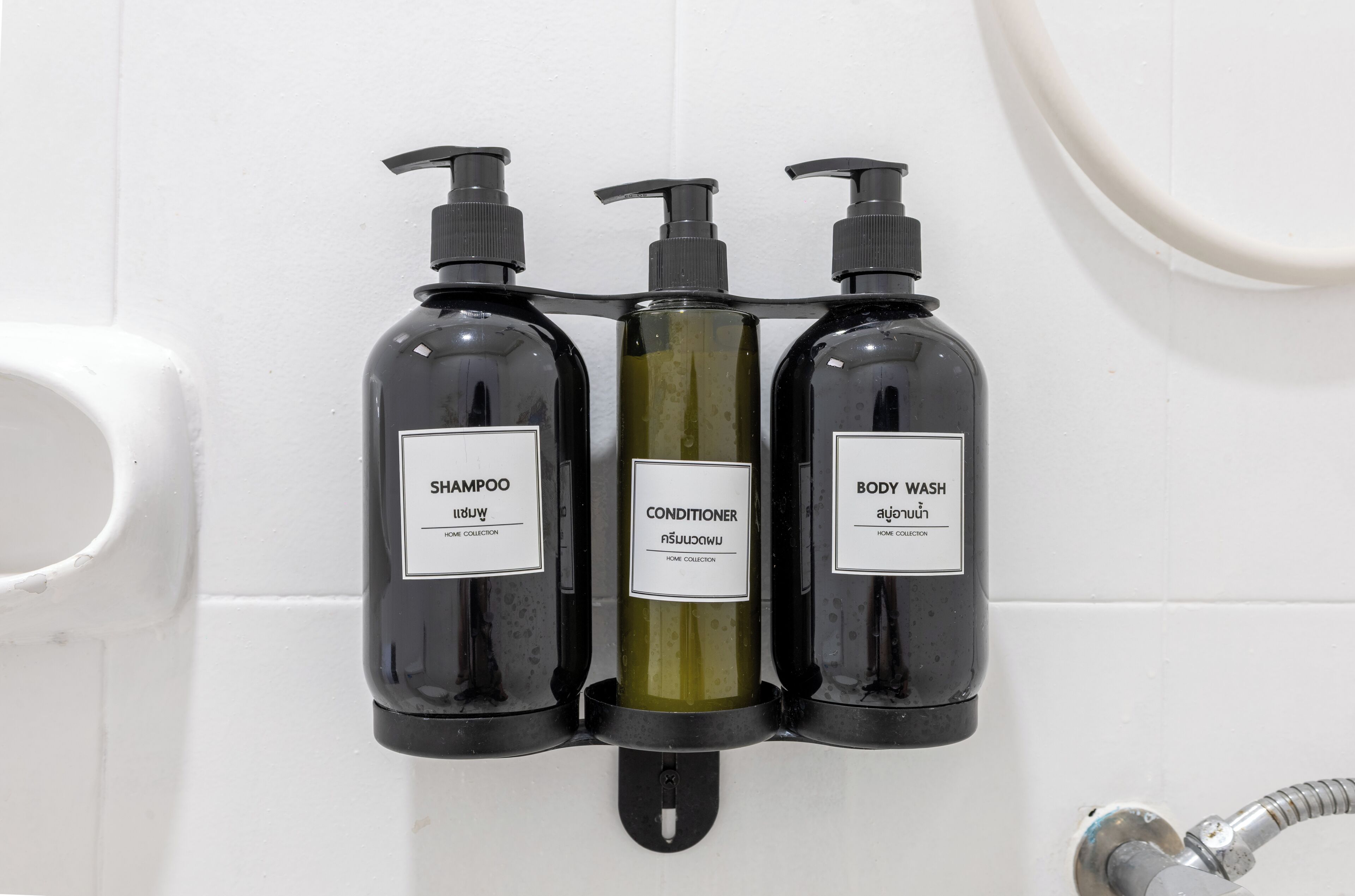 Three black bottles of shampoo, conditioner, and body wash mounted on a white tiled wall.