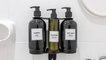 Three black bottles of shampoo, conditioner, and body wash mounted on a white tiled wall.
