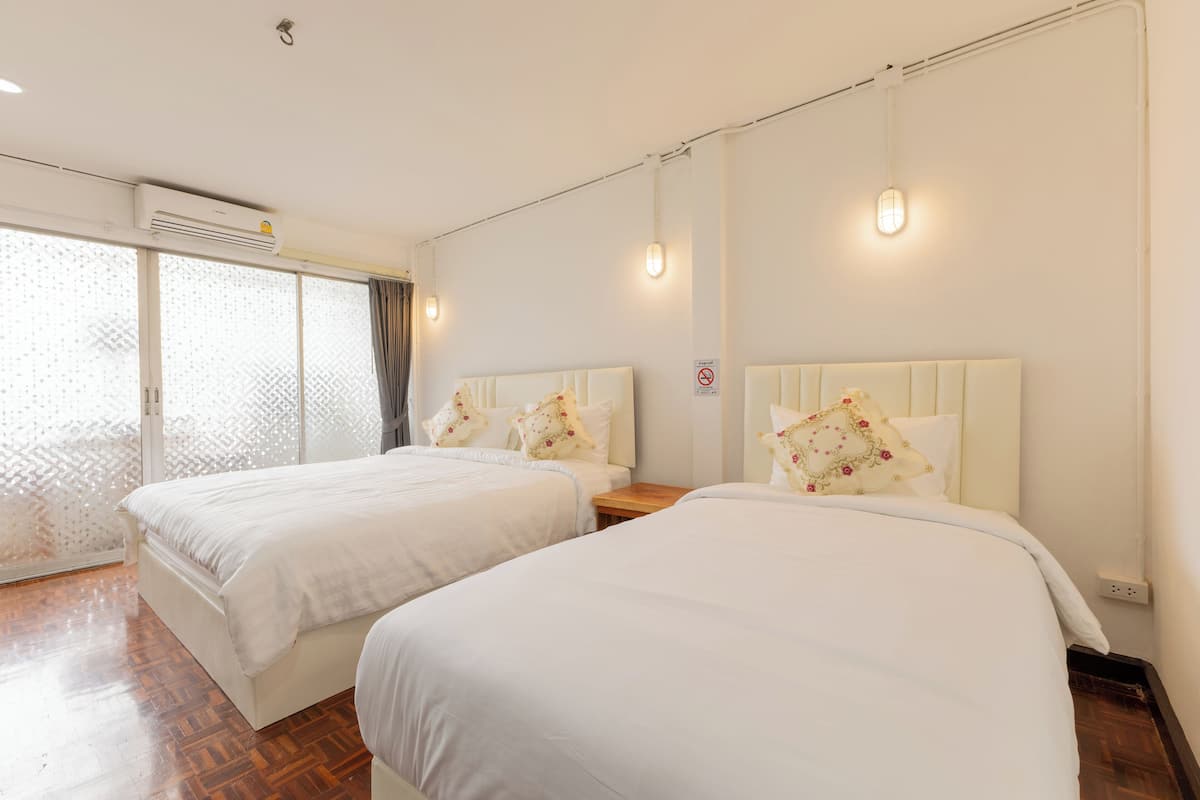 A hotel room with two beds, a large window with a view, and a wall-mounted air conditioner.