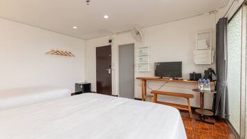 Une chambre d’hôtel avec deux lits, un bureau avec une télévision, un ventilateur et une fenêtre avec des rideaux.