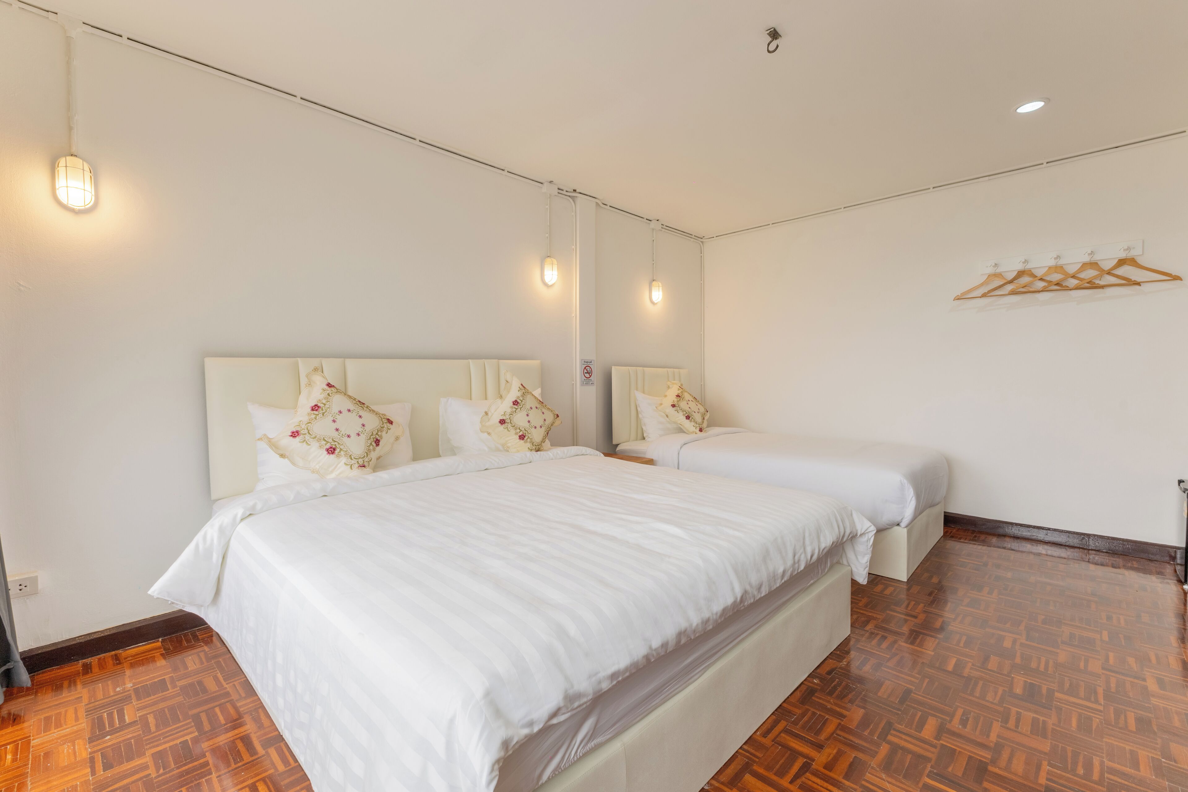 Habitación de hotel con dos camas, suelo de parquet de madera y perchero de pared.