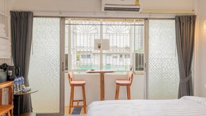 Hotelkamer met een bed, een kleine tafel met stoelen, een koffieapparaat en uitzicht op een gebouw door een raam met een metalen hek.