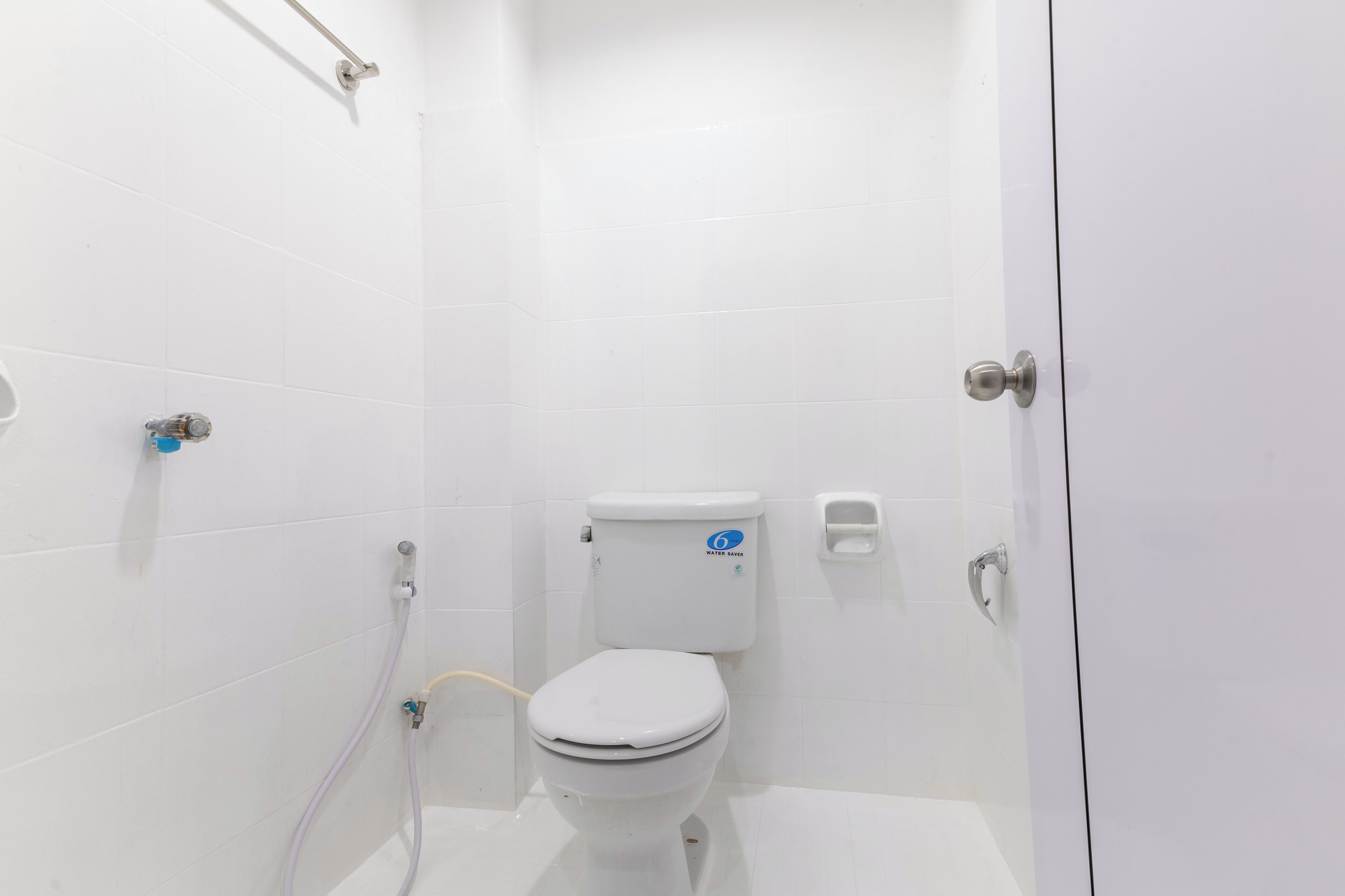 A small, white bathroom with a toilet, a hand dryer, and a shower area.