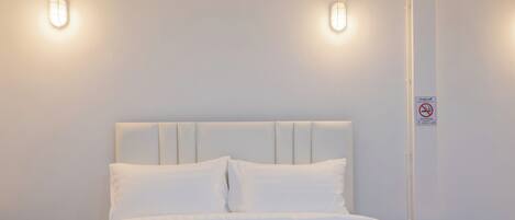 A neatly made bed with a white headboard and two bedside lamps.
