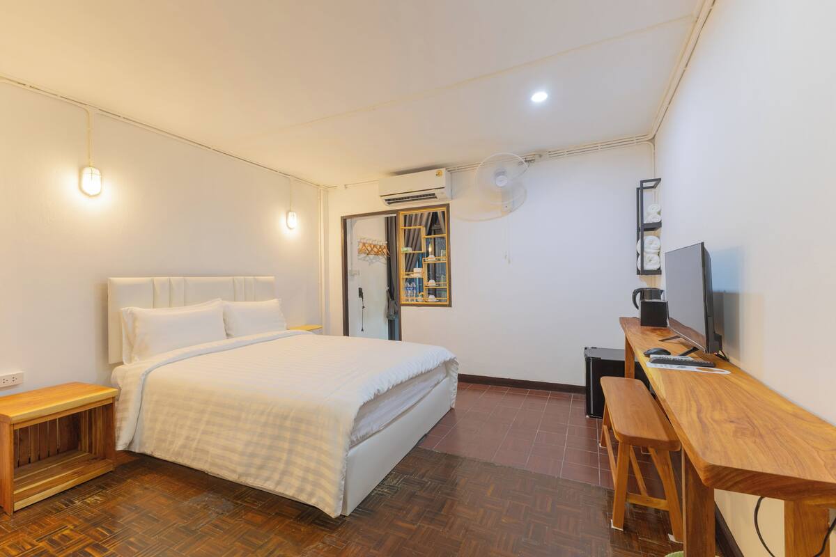 A bedroom with a bed, a wooden desk, a chair, a bench, and an air conditioning unit.