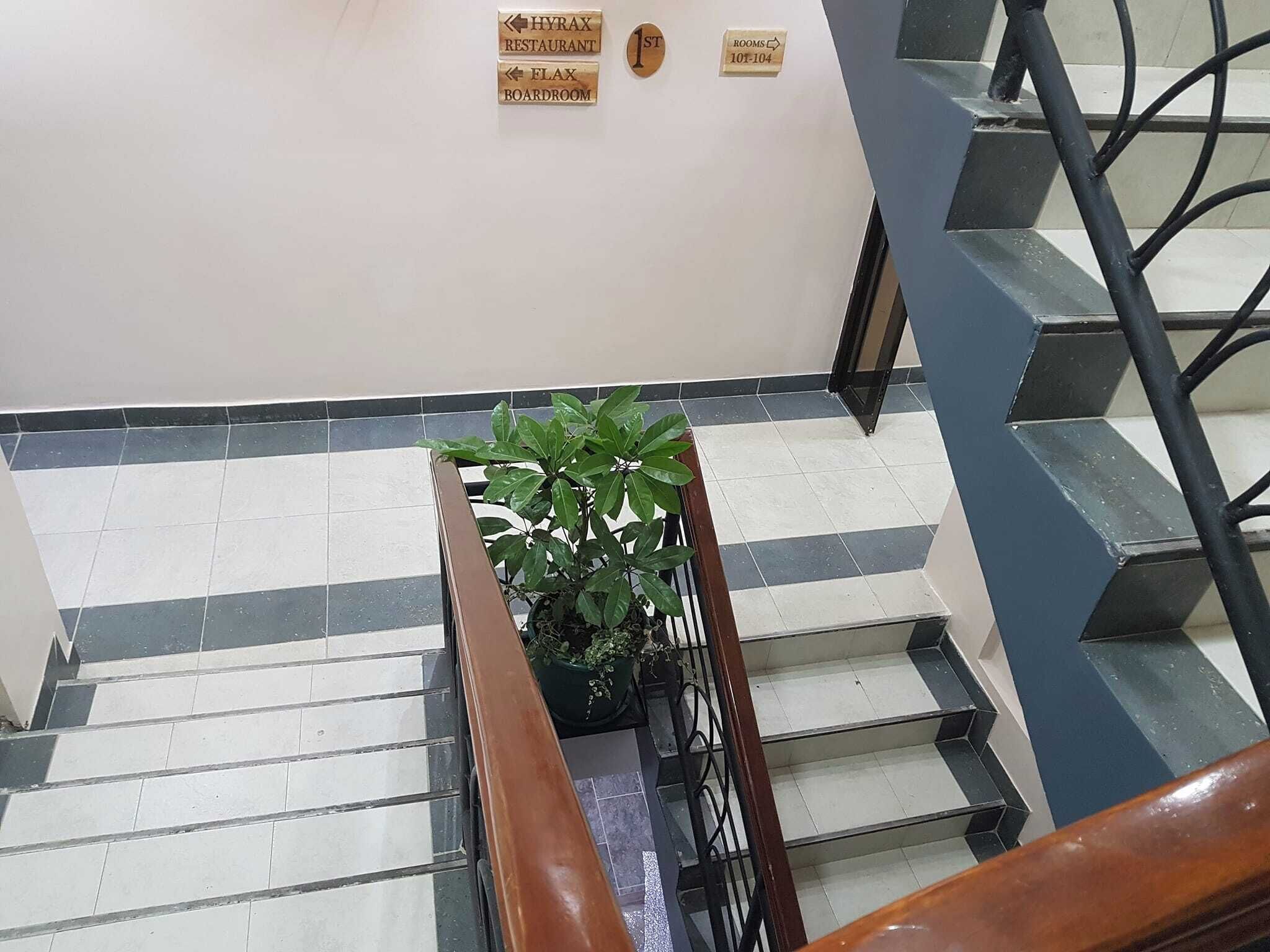 Una escalera con una planta en maceta, señales direccionales para el Restaurante Hyray y la Sala de Juntas Flax, y un cartel que indica la habitación 10-104.