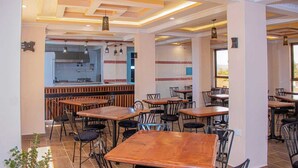 Un restaurant doté de plusieurs tables et chaises, d’un espace cuisine et offrant une vue sur l’extérieur.