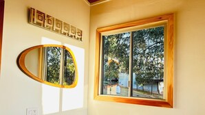 A bathroom with a white sink, a mirror with a wooden frame, and a window with a view of trees and a building.