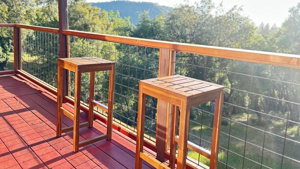 A wooden deck with two stools and a railing overlooking a forested area.