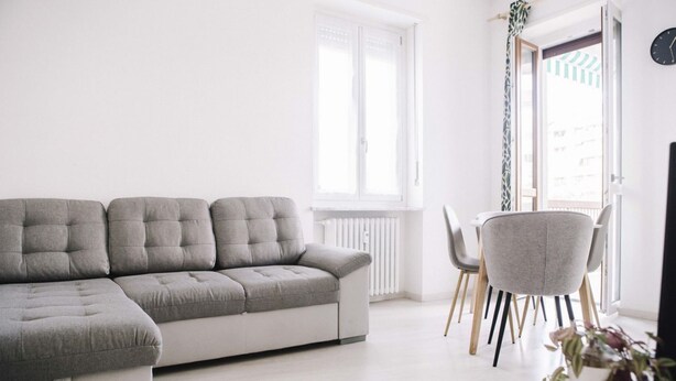 A modern living room with a grey sectional sofa, a dining table with chairs, and a window with curtains. - GuestHost - Borgo Filadelfia Apartment (Turin)