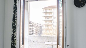 A balcony with a view of buildings, a clock on the wall, and a table with chairs. - GuestHost - Borgo Filadelfia Apartment (Turin)