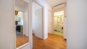Een gang met houten vloer, witte muren en een zichtbare badkamer met douche en wastafel.