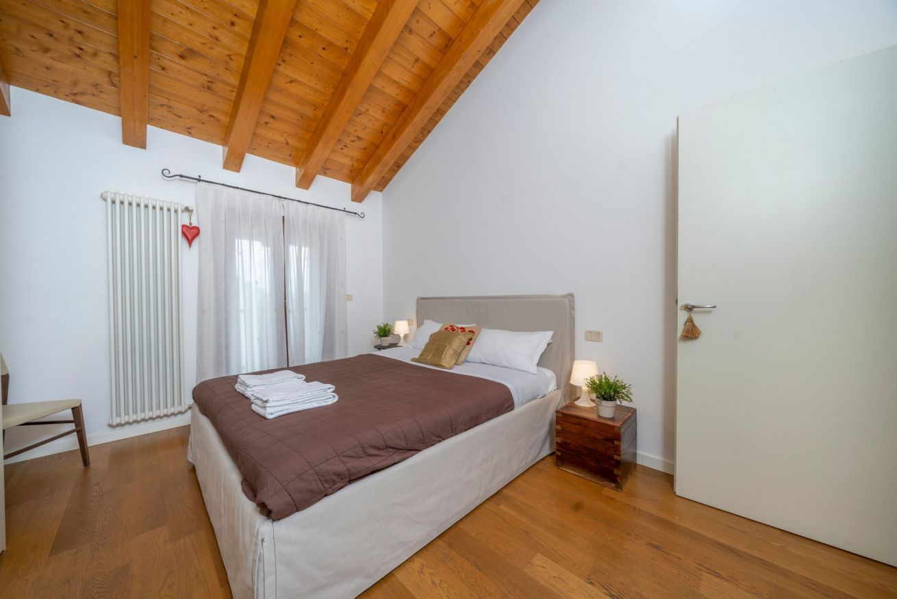 Un dormitorio con techo de madera, una cama con colcha marrón, una mesita de noche con lámpara, un radiador y una puerta.