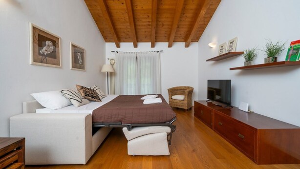 Een slaapkamer met een bed, een bank, een televisie, een houten kast en een rieten stoel.