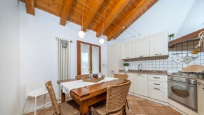 Een keuken met een houten plafond, witte kasten, een fornuis en een eettafel met rieten stoelen.