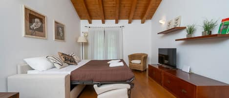 A bedroom with a bed, a sofa, a TV, a wooden cabinet, and a wicker chair.