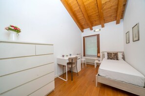 A bedroom with a bed, a desk, a chair, a radiator, and a window.