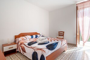 A bedroom with a bed, a nightstand, a chair, and a window with curtains.