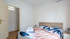 A hotel room with a bed, a nightstand, a lamp, and an air conditioning unit. - GuestHost - Cozy Flat in the Heart of Letojanni (Letojanni)