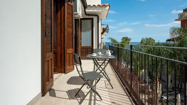 A balcony with a table and chairs, a door, and a view of the sea. - GuestHost - Cozy Flat in the Heart of Letojanni (Letojanni)